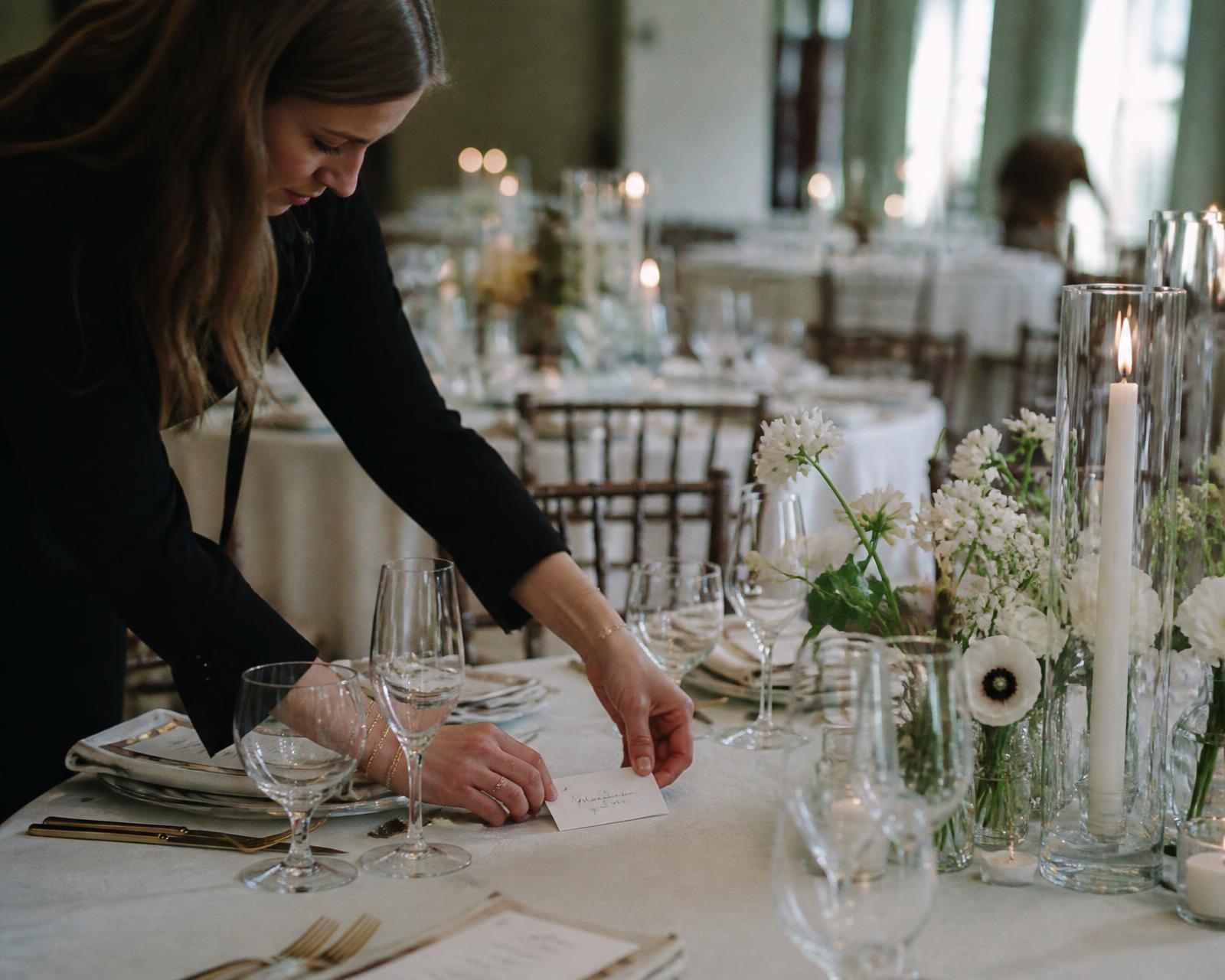 An event planner placing a handwritten place card on a table being finished before guests arrive